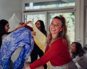 Studentin tanzt mit bunten Tüchern gemeinsam mit ihren Kommiliton:innen