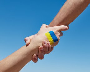 Zwei Hände greifen sich gegenseitig mit einer Ukraine Flagge auf dem Handrücken