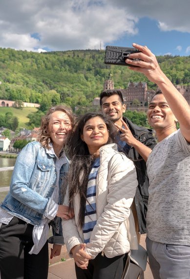 Studierende auf der Alten Brücke in Heidelberg, welche gerade ein Selfie mit Blick auf das Heidelberger Schloss schießen.