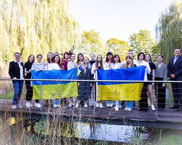 18 Ukrainerinnen studieren aktuell an der SRH Hochschule Heidelberg. Im Science Garden der Hochschule halten sie die ukrainische Flagge hoch.