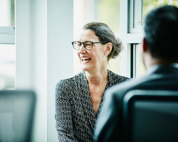 Frau mit Brille lacht während eines Gesprächs