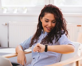 Sitzende Frau schaut auf ihre Armbanduhr