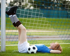 Eine Fußballspielerin liegt entspannt im Tor, die Beine an den Pfosten gelehnt.