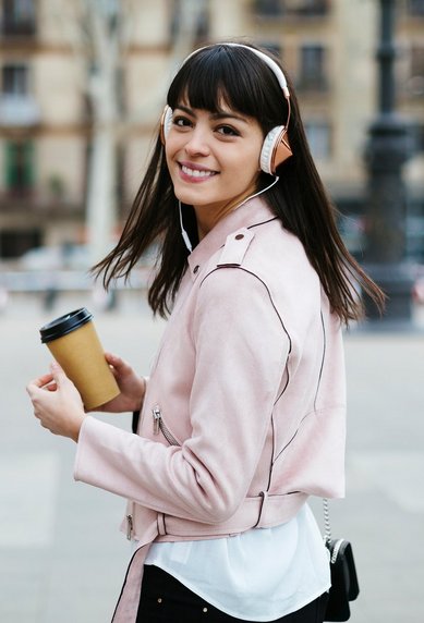 Studentin trägt Kopfhörer und hält einen Kaffeebecher in der Hand
