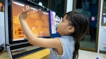 Kleines Mädchen mit Hörschädigung spielt an einem Bildschirm 