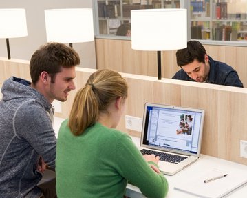 Studenten recherchieren am Laptop an einem Arbeitsplatz in der Bibliothek.