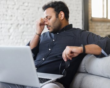 Ein Mann am Laptop hält sich müde die Hand an den Kopf.
