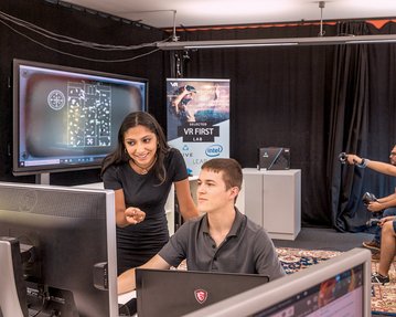 Studenten arbeiten am PC während dahinter ein VR Spiel am Bildschirm getestet wird.