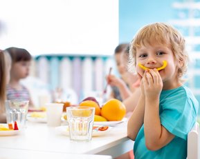 Ein blonder Junge hält sich eine gelbe Paprika vor den Mund