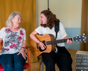 Junge Frau spielt Guitarre und singt gemeinsam mit einer alten Dame