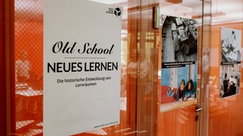 Ein Poster zum Thema "Neues Lernen" hängt an einer Glasscheibe.